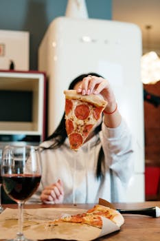 Woman enjoying a slice of pepperoni pizza and a glass of red wine at home.