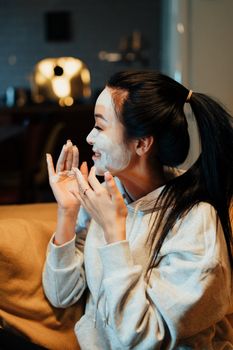 在舒适的夜晚，一位亚洲女性戴着护肤口罩在家放松，享受自我护理的仪式
