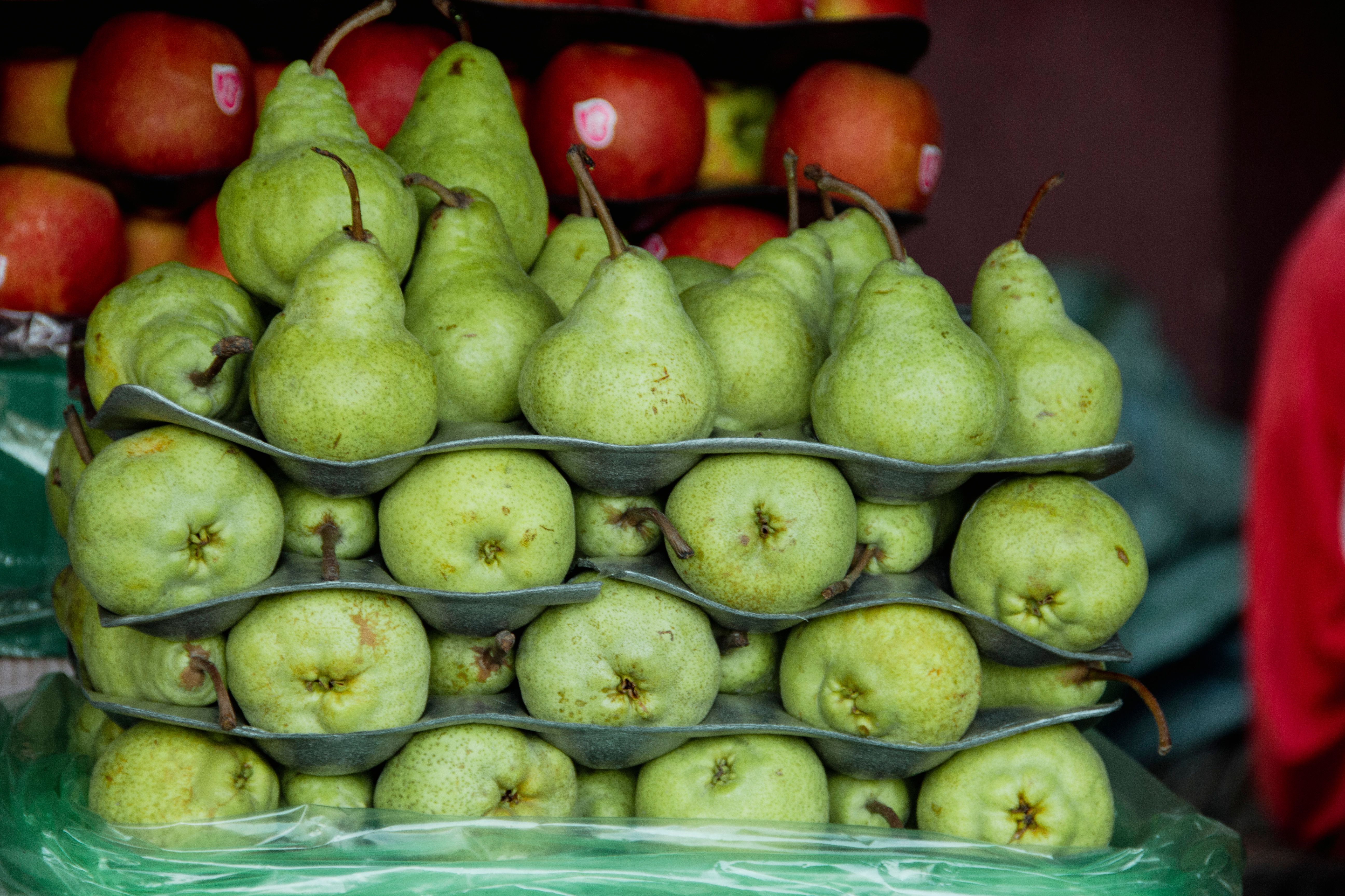 Close-up of ripe green pears neatly stacked in cartons at a market with apples in the background.