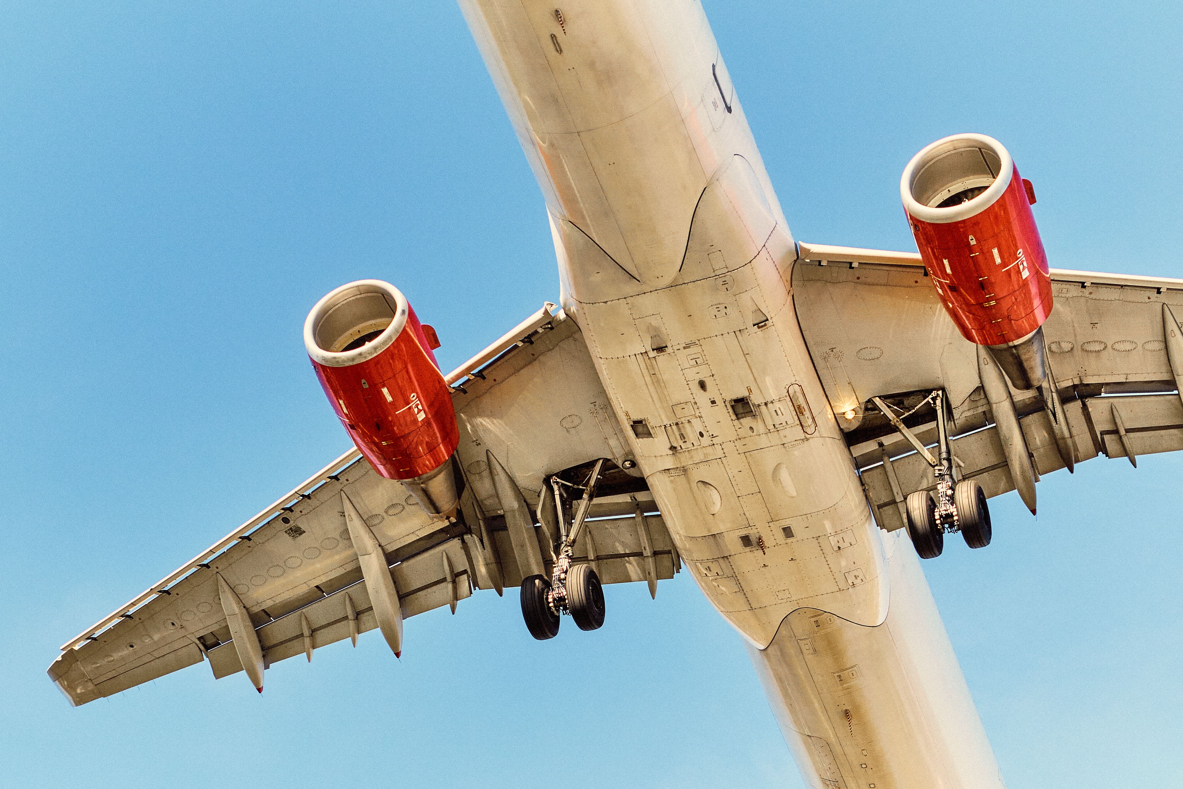 Dynamic shot of an airplane flying with visible undercarriage and engines against a clear blue sky.
