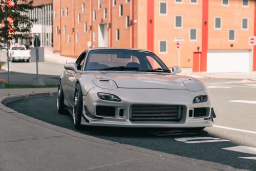 Free Photo of a white sports car parked on an urban street with red brick buildings in the background. Stock Photo