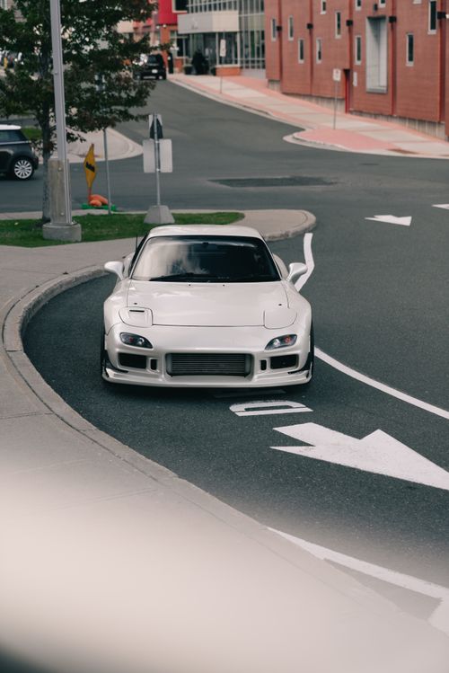 Free A sleek white sports car rounding a city street corner, showcasing modern automotive design. Stock Photo