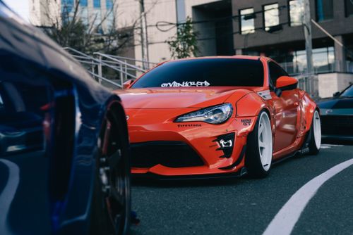 Free Vibrant orange sports car parked in urban area with stylish modifications and white rims. Stock Photo