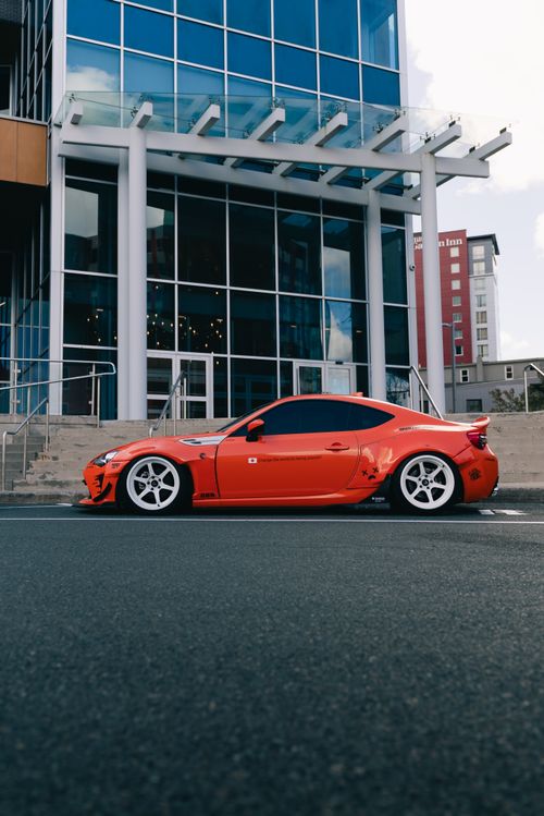 Free A vibrant red sports car parked in front of a modern glass building. Stock Photo