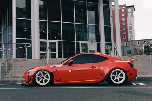 Free Sleek orange sports car parked outside a modern building in an urban area. Stock Photo