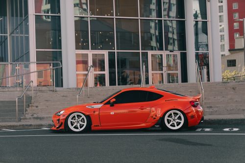 Free Bright orange sports car parked in front of a modern building, showcasing urban street style. Stock Photo