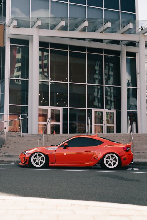 Free Sleek red sports car parked in front of a modern urban building, showcasing style and design. Stock Photo