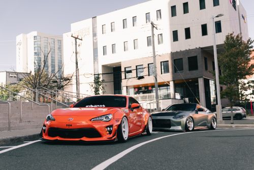 Free Two modified sports cars parked street-side in a modern urban setting, showcasing automotive style. Stock Photo