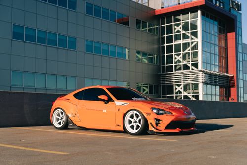 Free Vibrant orange sports car parked beside a modern glass building in daylight. Stock Photo