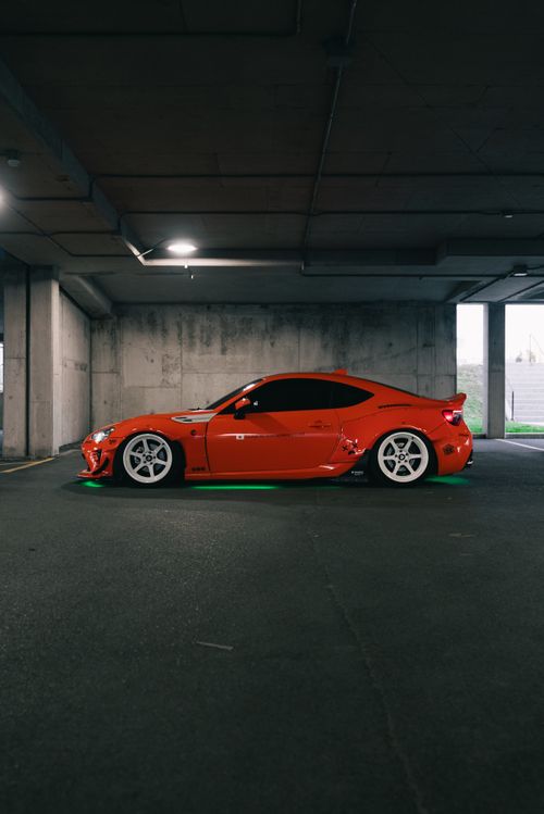 Free A striking orange sports car parked in a dimly lit urban garage, featuring neon underglow. Stock Photo