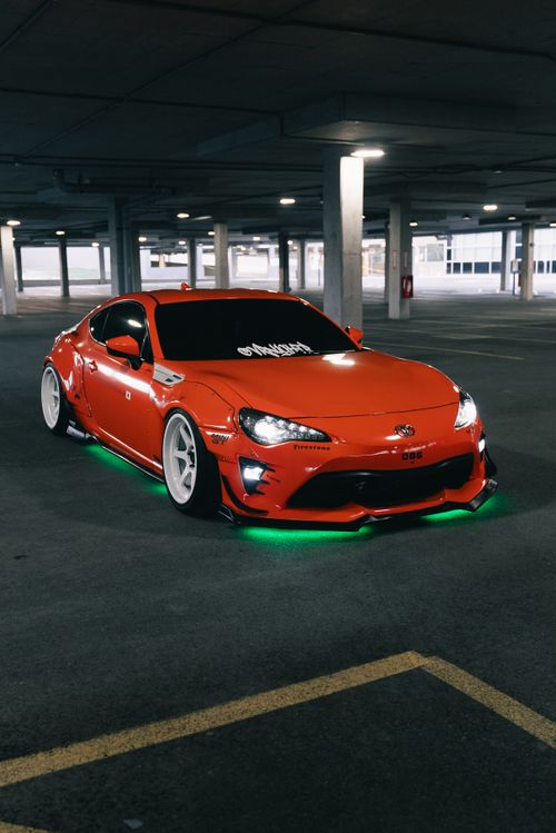 Free Sleek modified red sports car with green neon lights in an underground garage setting. Stock Photo