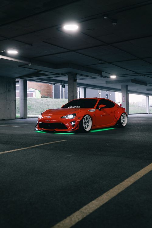 Free Dynamic shot of a modified red sports car with neon lights in an urban parking garage. Stock Photo