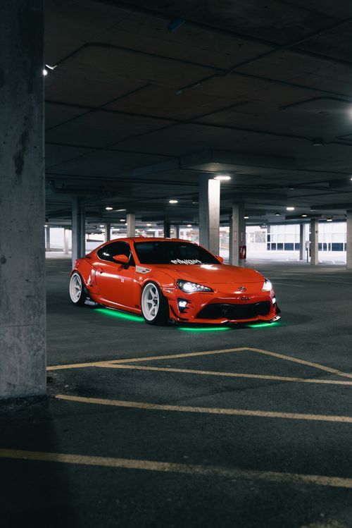 Free An orange sports car with custom lights parked in a dimly lit urban garage. Stock Photo
