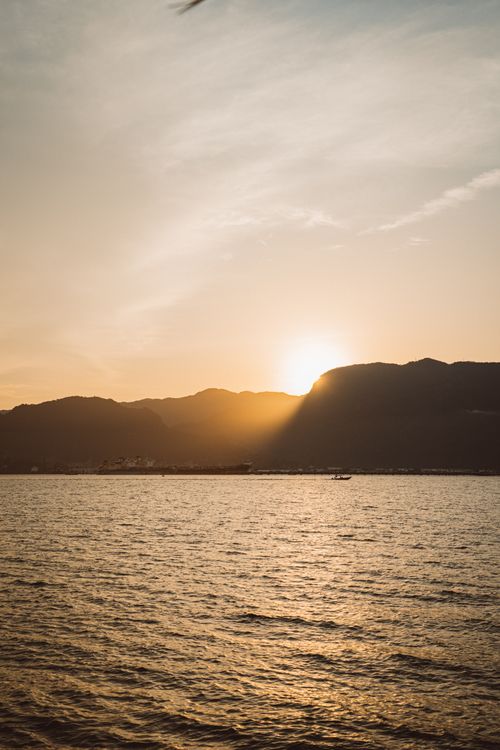 Free A peaceful sunset casting warm hues over the ocean and silhouetted mountains in the distance. Stock Photo