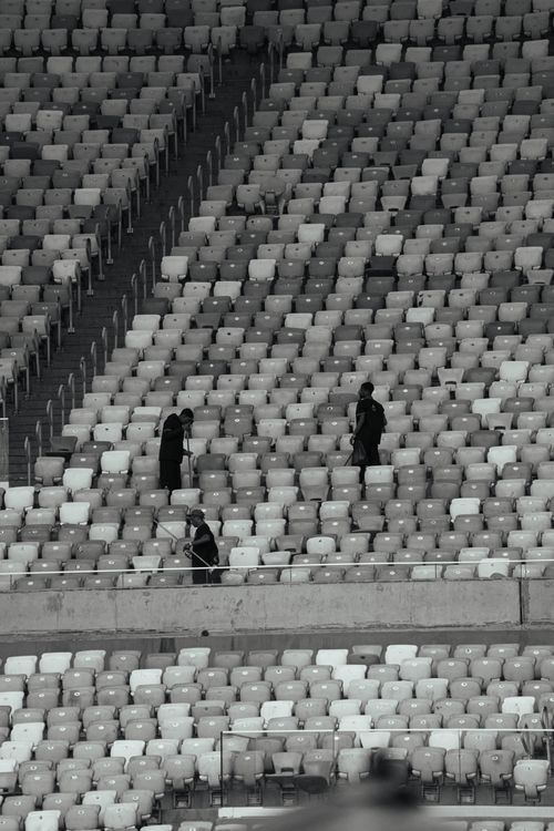 Free Minimalistic black and white photo of a mostly empty stadium with few people. Stock Photo