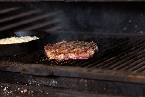 Free Juicy steak grilling on an outdoor barbecue with a skillet nearby. Smoky and appetizing. Stock Photo