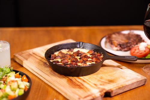 Free Deliciously prepared dish served in an iron skillet with side salad and drink, set on a wooden table. Stock Photo