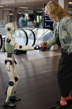 A woman engaging in a playful gesture with a humanoid robot indoors.