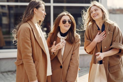 Free Cheerful female friends with long hair in elegant coats smiling while happily chatting with each other on street Stock Photo