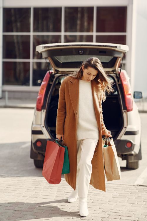 Free Full body stylish lady in elegant clothes and coat walking along street holding paper bags after shopping in city center Stock Photo