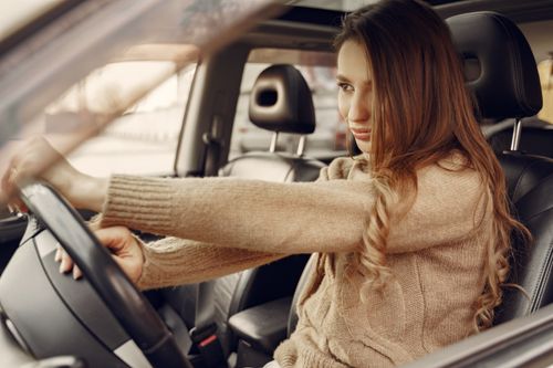 Free Side view of concentrated contemporary female driver in casual clothes going along street road alone by car with leather interior Stock Photo