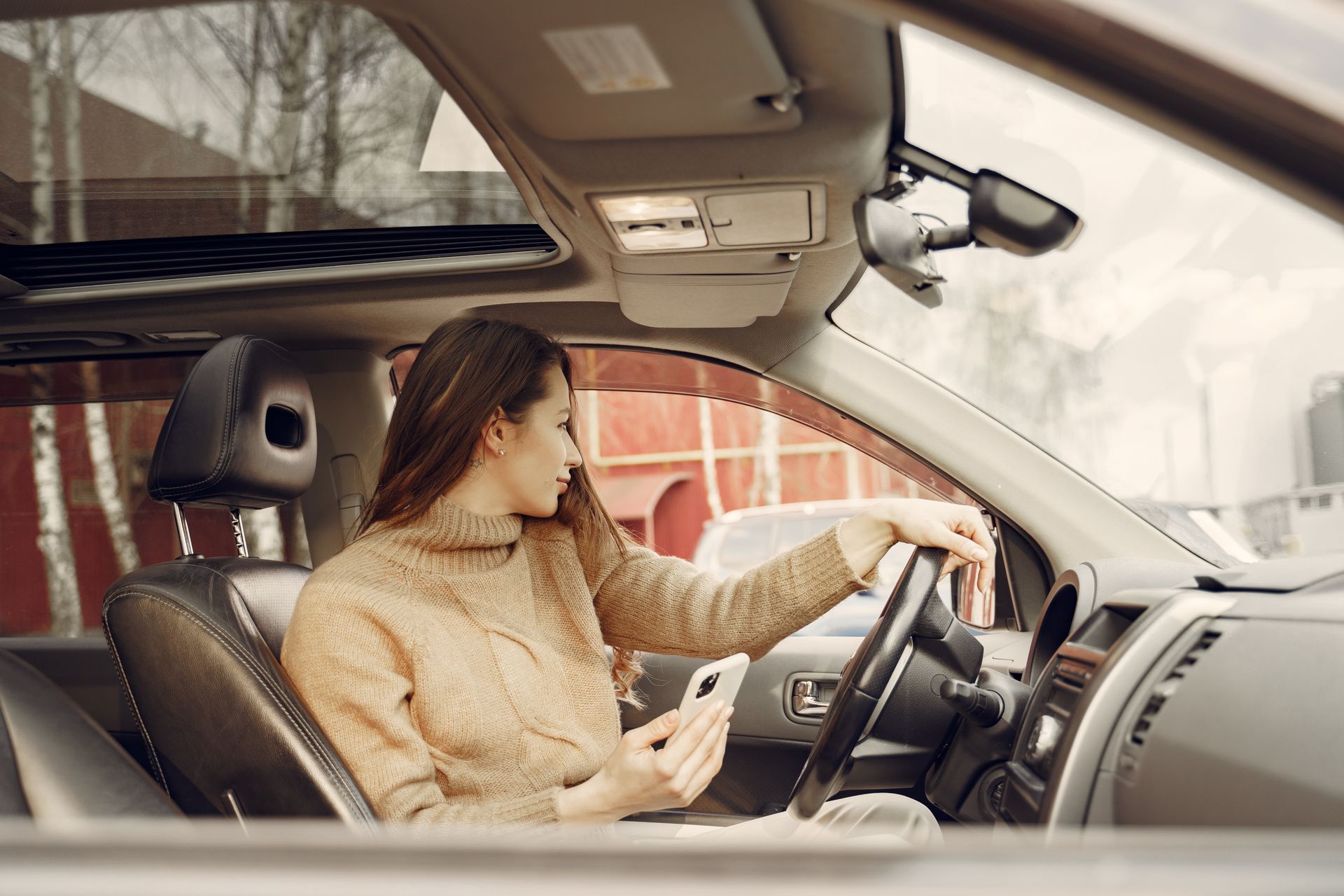 A woman inside a car glances at her smartphone, depicting modern connectivity and lifestyle.