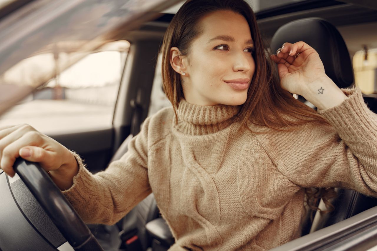 positive young female driver in warm clothes at wheel of leather inter