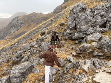 Two hikers traverse a rocky mountain path on a cloudy day, showcasing adventure in nature.