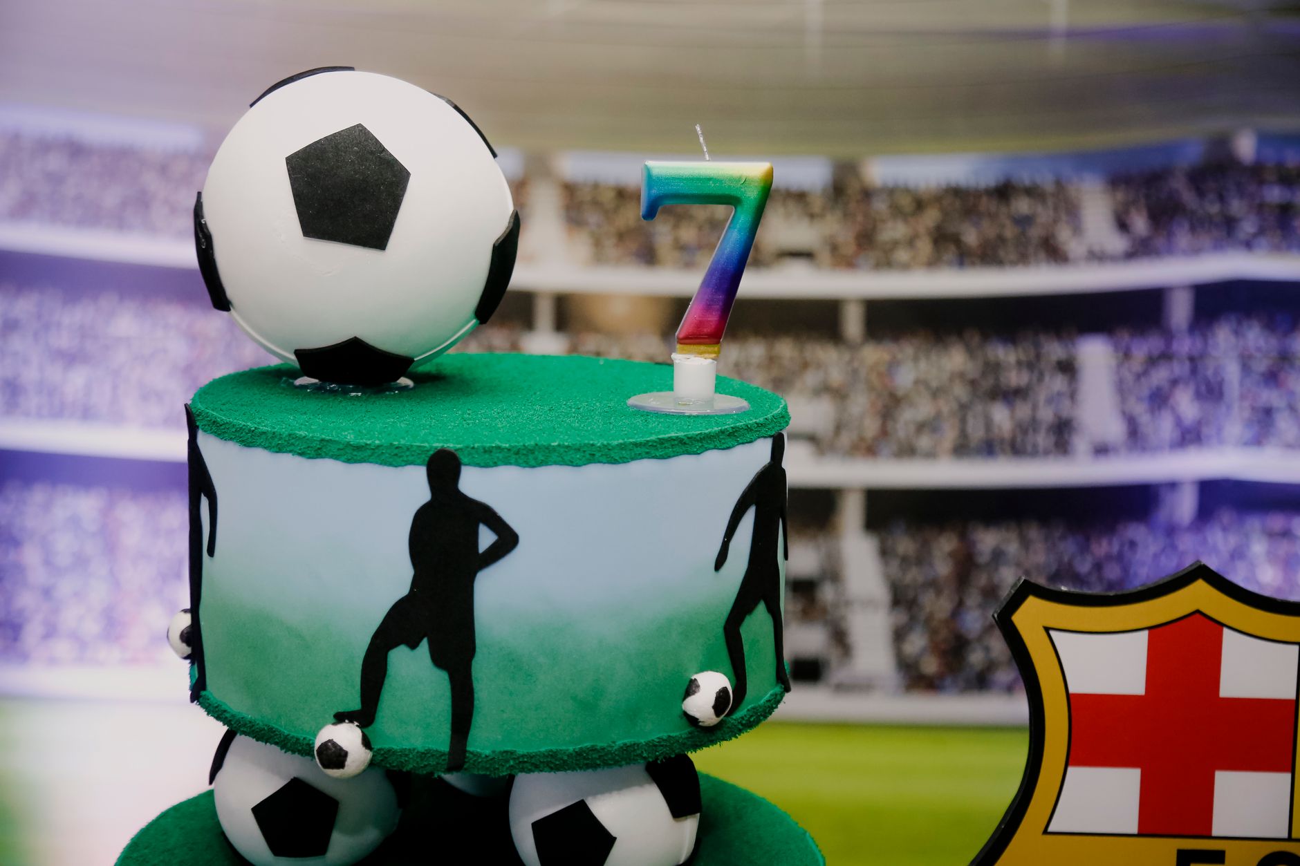 A two-tiered soccer-themed cake with a rainbow number seven candle, perfect for a football fan's birthday.
