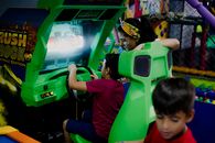 Anonymous boy playing car racing simulator near mother and sibling