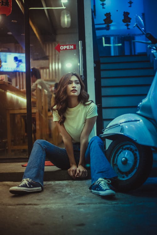 Woman In White Shirt And Blue Denim Jeans Sitting On Sidewalk 