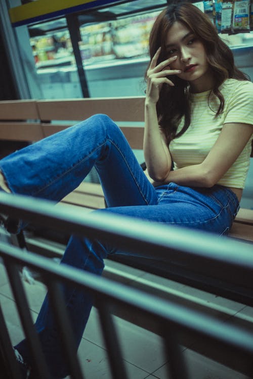 Woman In A T-shirt And Blue Denim Jeans Sitting On A Bench