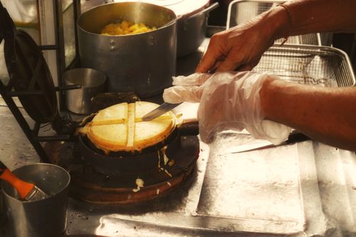 Free Street vendor cuts hot pancakes on griddle. Close-up action shot showcasing traditional food preparation with warm tones. Stock Photo