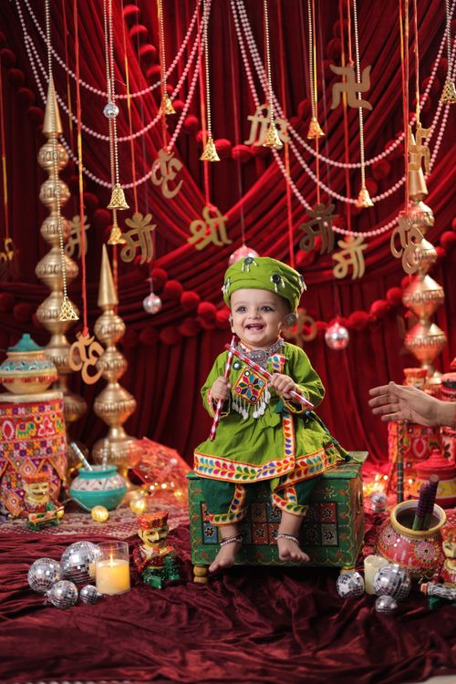 Free A joyful baby dressed in vibrant traditional Indian clothing amidst a colorful, festive setting. Stock Photo