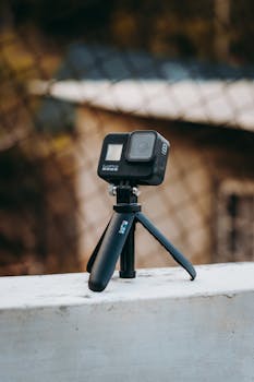 Portable action camera mounted on a mini tripod with blurred background in daylight.