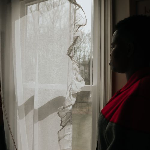 Free A thoughtful woman standing by a window, gazing outside in soft light, creating a serene and introspective mood. Stock Photo