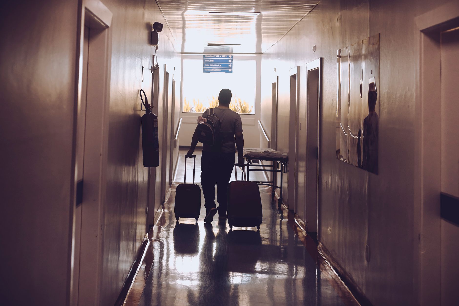 Silhouette of a traveler with luggage walking down an illuminated hotel corridor.