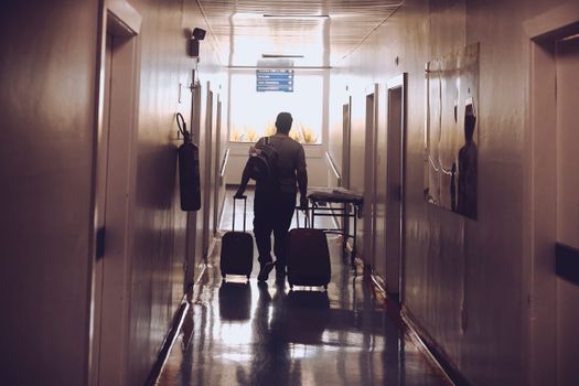 Silhouette of a traveler with luggage walking down an illuminated hotel corridor.
