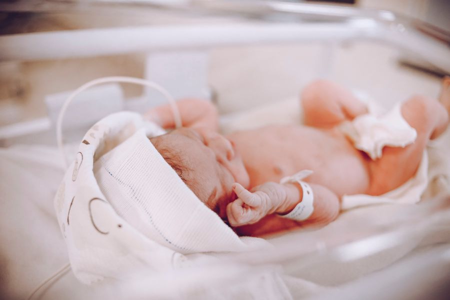 A newborn baby swaddled in a blanket resting in a hospital crib