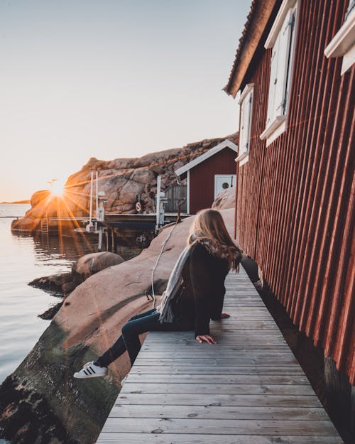 Unrecognizable woman admiring seascape in sunshine near house on platform