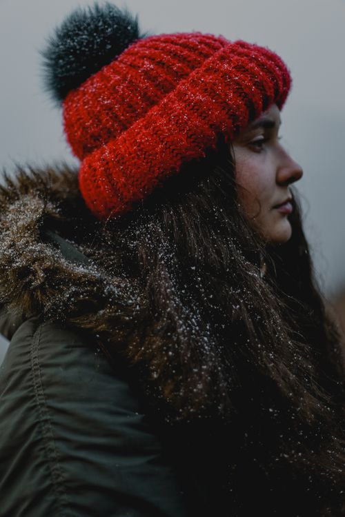 Free Side profile of a woman wearing a red knitted hat and coat with fur hood in winter." Stock Photo