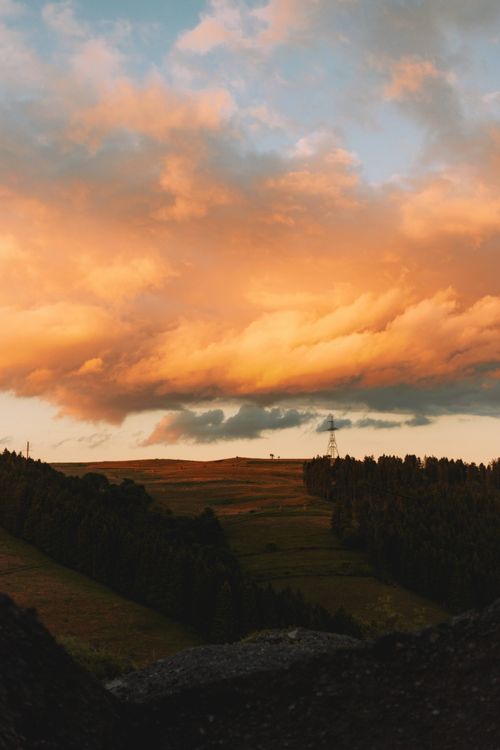 Free A breathtaking sunset casting warm hues over lush rolling hills and rustic powerlines. Stock Photo