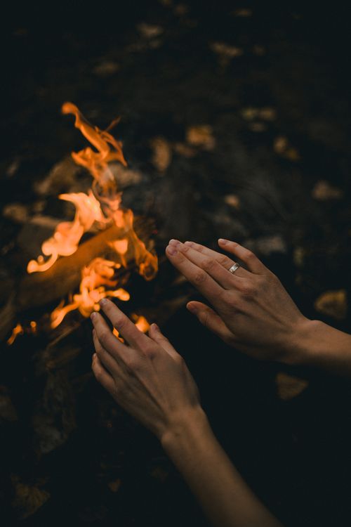 Free Close-up of hands warming over a campfire at night, with a dark, moody atmosphere. Stock Photo