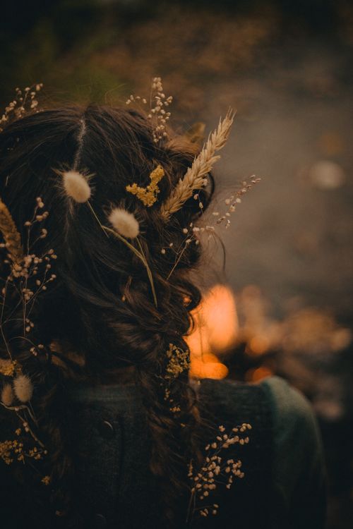 Free Back view of a person with a braid adorned with dried flowers, lit by warm firelight. Stock Photo