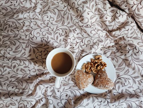 Free Heart-shaped pastries and walnuts on plate with coffee on patterned bedding. Cozy breakfast scene. Stock Photo
