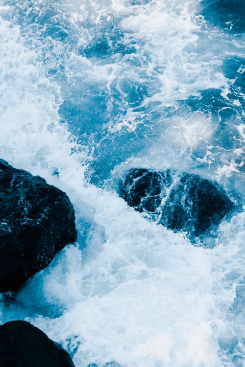 Free Vibrant ocean waves crash against dark rocks in a dramatic seascape shot. Stock Photo