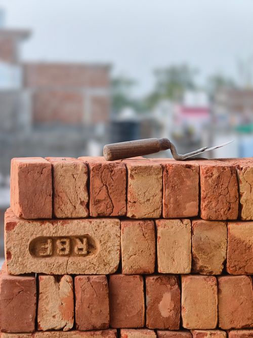 Free Stack of red clay bricks with a mortar trowel on top, set outdoors. Perfect for construction themes. Stock Photo