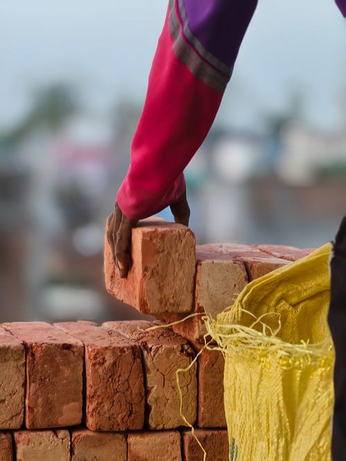 Free Close-up of a worker's hand placing a brick on a wall at a construction site. Stock Photo