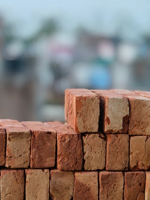 Free A close-up view of stacked red clay bricks with a blurred urban background. Stock Photo
