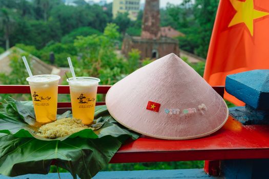 Traditional Vietnamese setting with conical hat, iced tea, and noodles, featuring national flag.